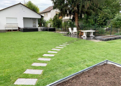 Garten mit großer Rasenfläche über die ein Steinplattenweg führt zu einer Steinterrasse