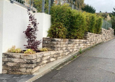 Mauer aus hellen Steinen als Begrenzung zum garten mit Sträuchern und Büschen als Sichtschutz